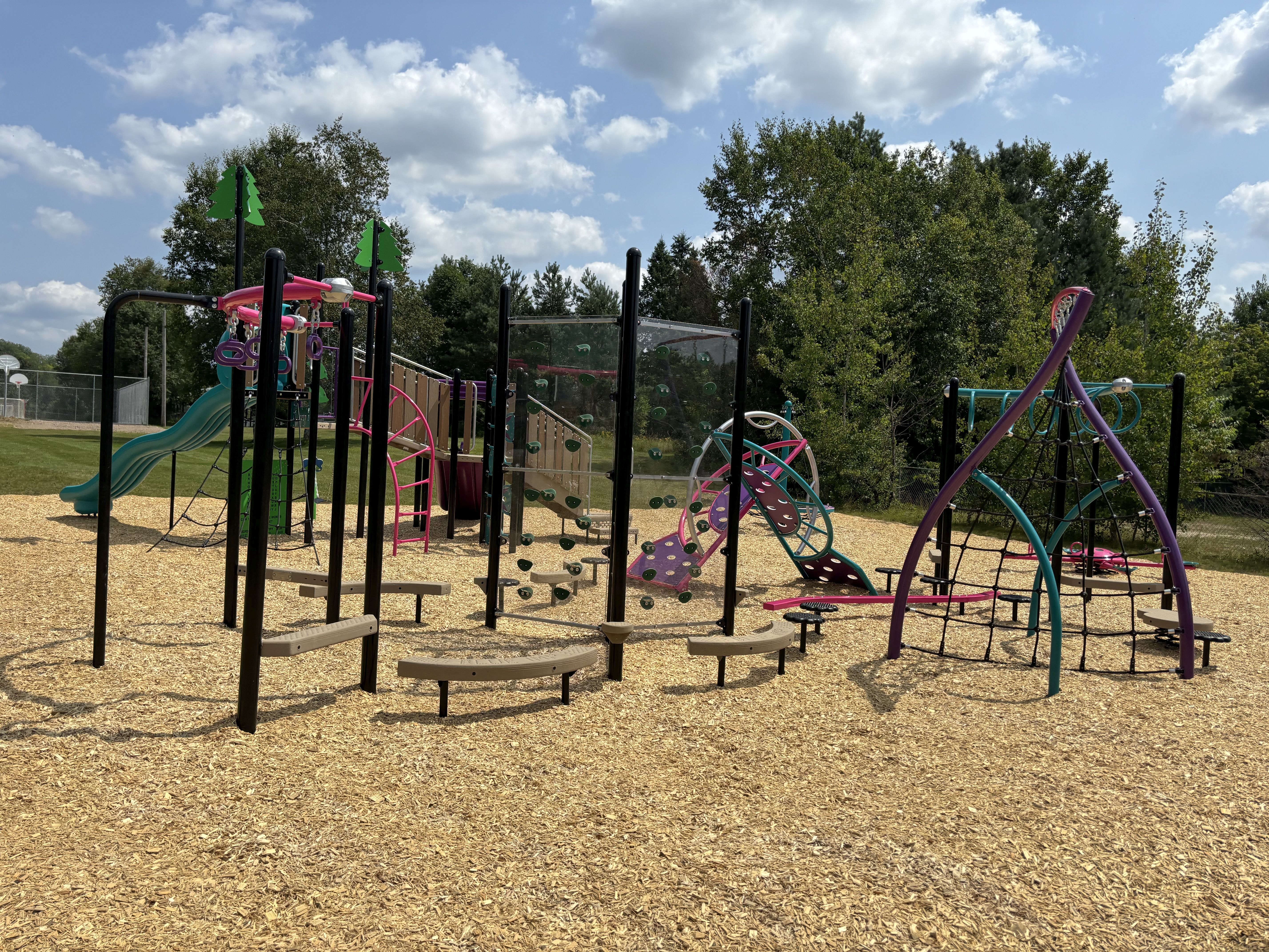 Bright, colourful playground with pinks, purples, teal, tan colours. Shows a climbing aparatus, slides.